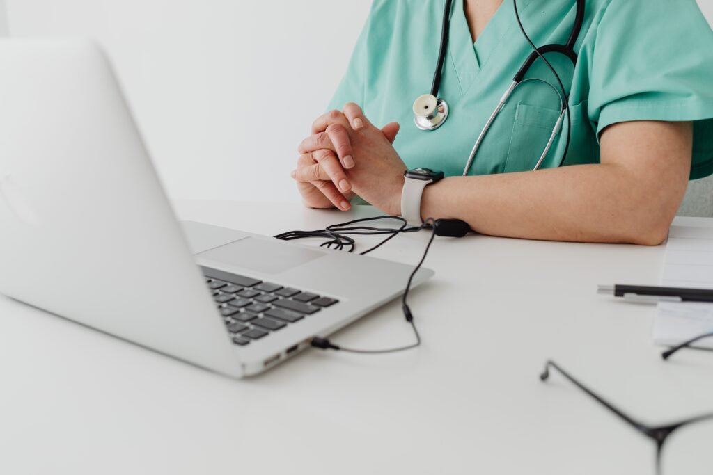 Medical practitioner in scrub suit using a laptop for remote consultation and documentation.